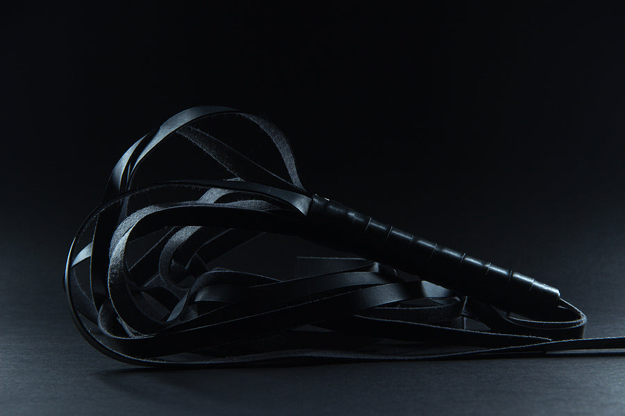 Bondage & Kink: Black whip lying on a dark surface, perfect for enhancing BDSM experiences and play.