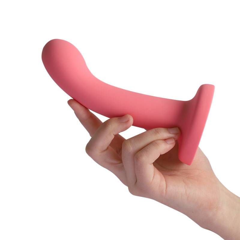 A hand holding a pink FlexDong vibrating strap-on dildo, showcasing its smooth design and angled tip.