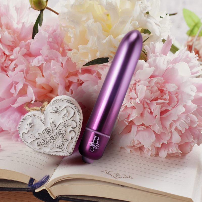 Boudoir Parlour Prince bullet vibrator next to flowers, showcasing a waterproof bullet vibrator in vibrant purple.