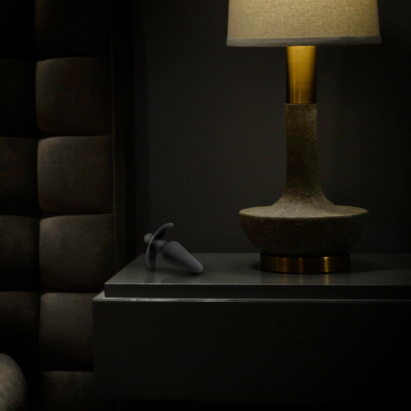 Anal Adventures Platinum Vibrating Plug next to a lamp on a nightstand, showcasing the vibrating butt plug.