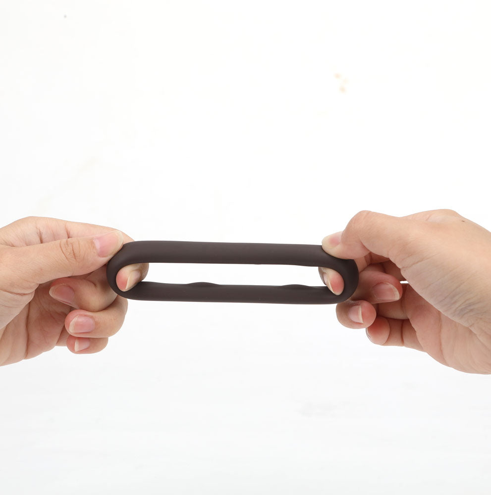 Maia GUNNER - Chocolate - Dark  Cock Ring shown being stretched by hands, highlighting its flexibility and durability.