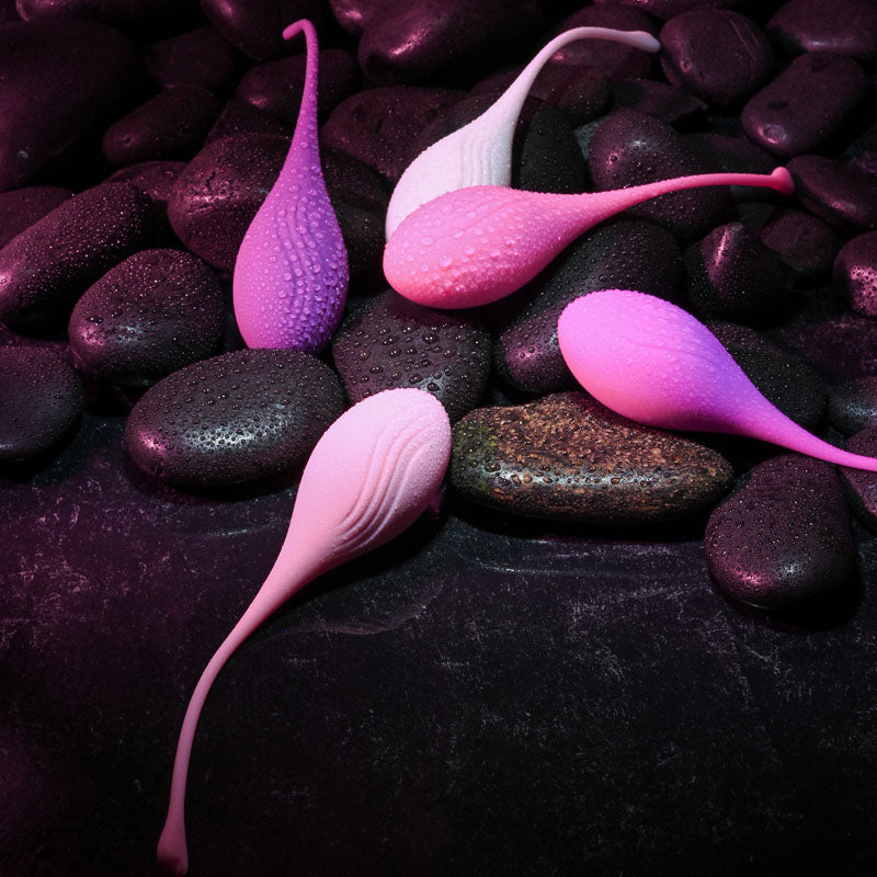 Evolved TIGHT & DELIGHT - Kegel Trainer Set - 5 Piece Kit displayed with colorful kegel balls on dark stones.