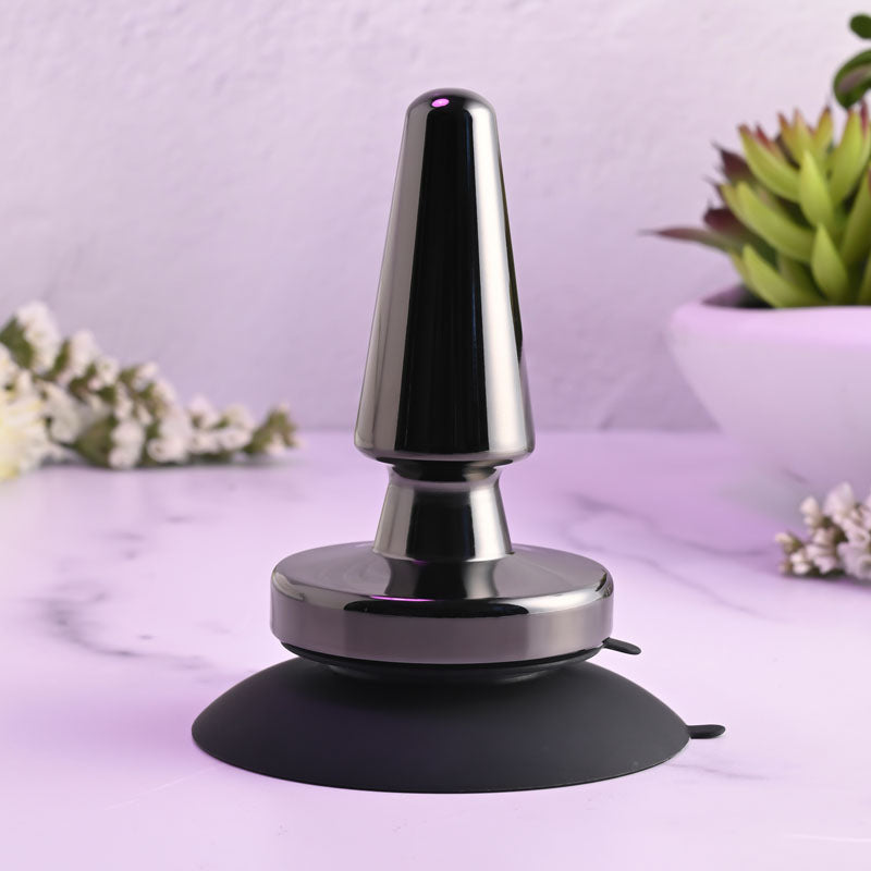 Evolved BEGINNER METAL PLUG - Black 11.2 cm USB Rechargeable Vibrating Butt Plug on a marble surface with plants.