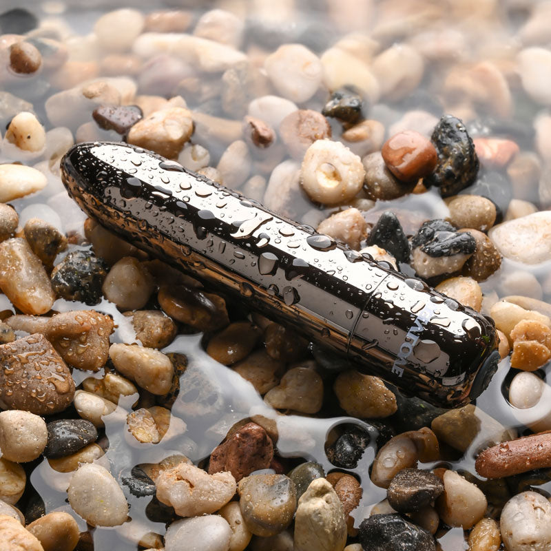 Evolved REAL SIMPLE - Black 10 cm USB Rechargeable Bullet on pebbles with water droplets.