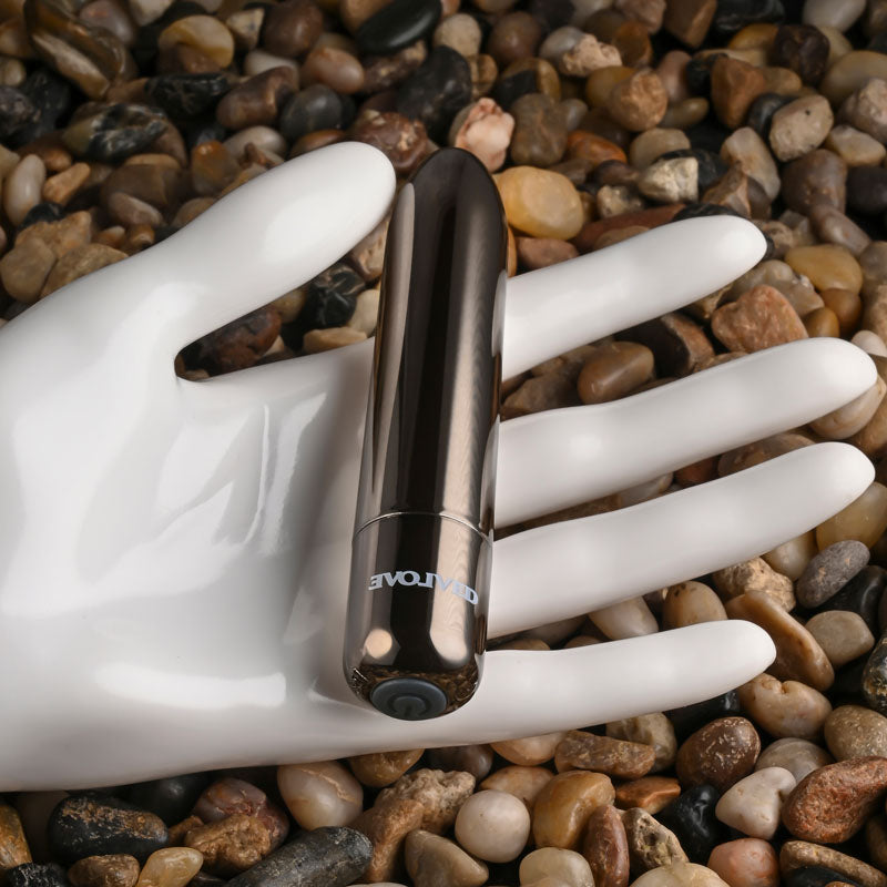 Evolved REAL SIMPLE - Black 10 cm USB Rechargeable Bullet on a hand, surrounded by smooth pebbles.