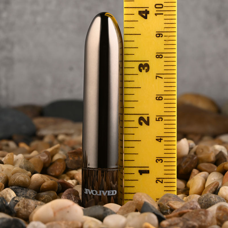 Evolved REAL SIMPLE - Black 10 cm USB Rechargeable Bullet next to a ruler on smooth pebbles for size comparison.