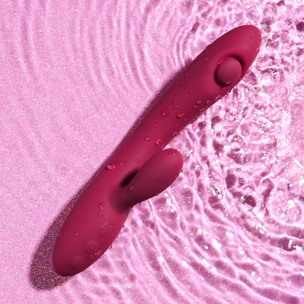 Evolved JAMMIN' G - Burgundy 20.1 cm USB Rechargeable Rabbit Vibrator lying on pink surface with water droplets.