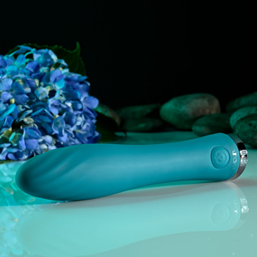 Evolved ULTRA WAVE - 13 cm USB Rechargeable Mini Vibrator in teal color beside blue flowers.