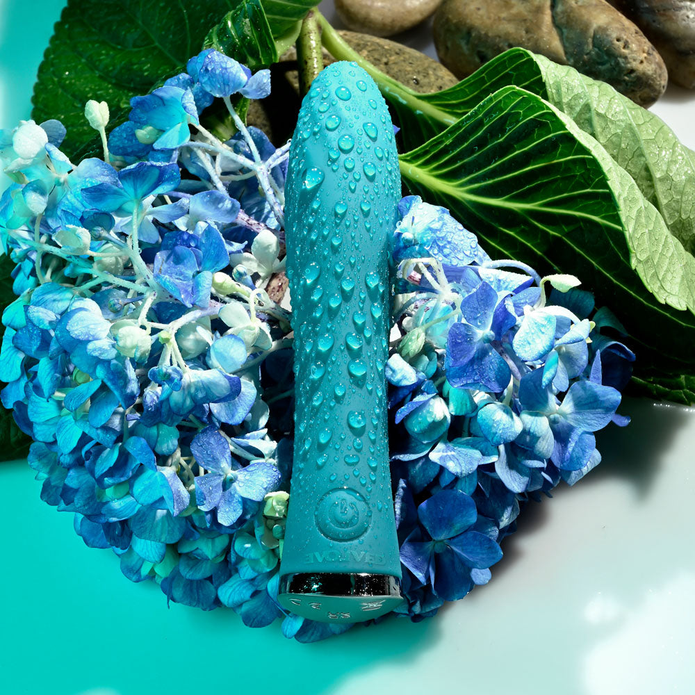 Evolved ULTRA WAVE -  13 cm USB Rechargeable Mini Vibrator on blue flowers with water droplets.