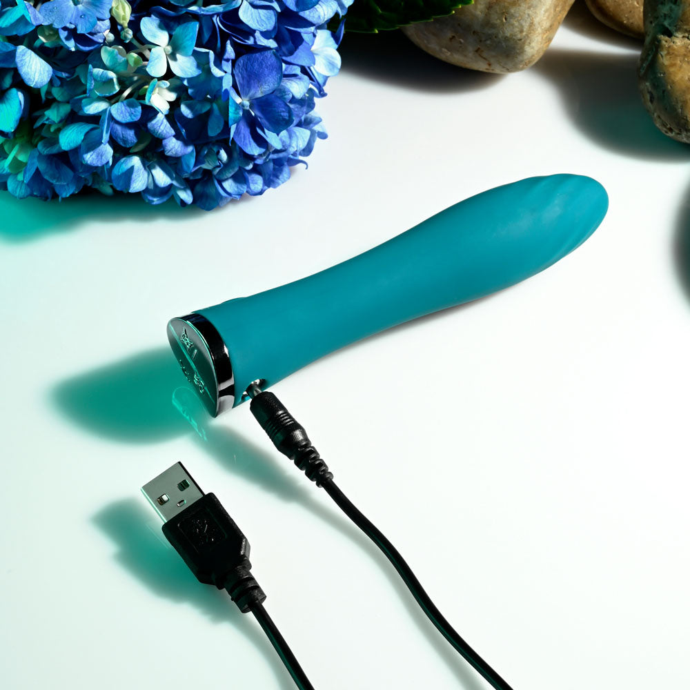 Evolved ULTRA WAVE -  13 cm USB Rechargeable Mini Vibrator on a table with a USB charger, surrounded by flowers.