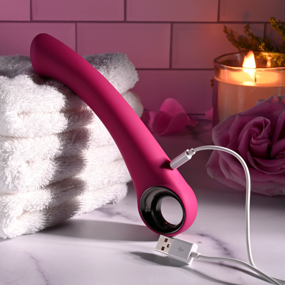 Evolved PLEASURE CURVE - 19 cm USB Rechargeable Vibrator charging next to towels and candles.