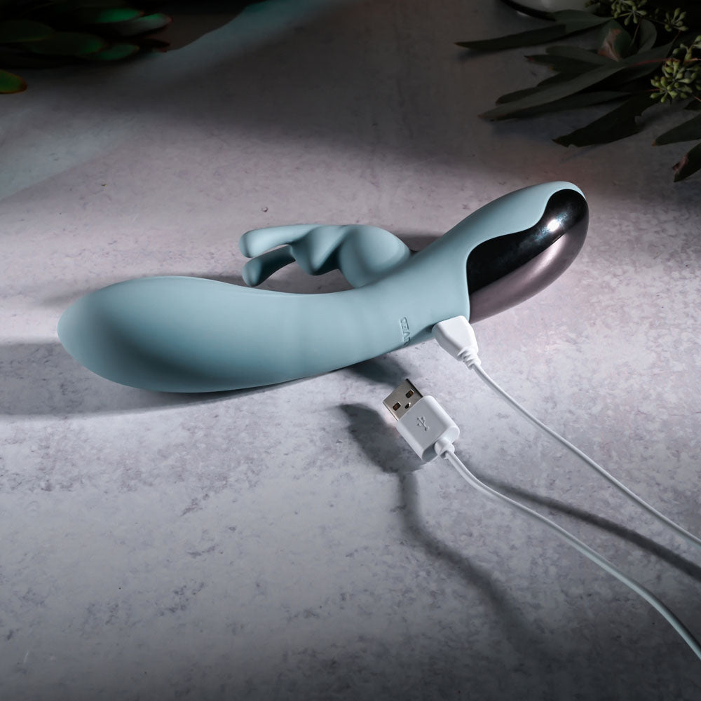 Evolved BOSS BUNNY - Baby 20.1 cm USB Rechargeable Rabbit Vibrator charging with USB cable on a textured surface.
