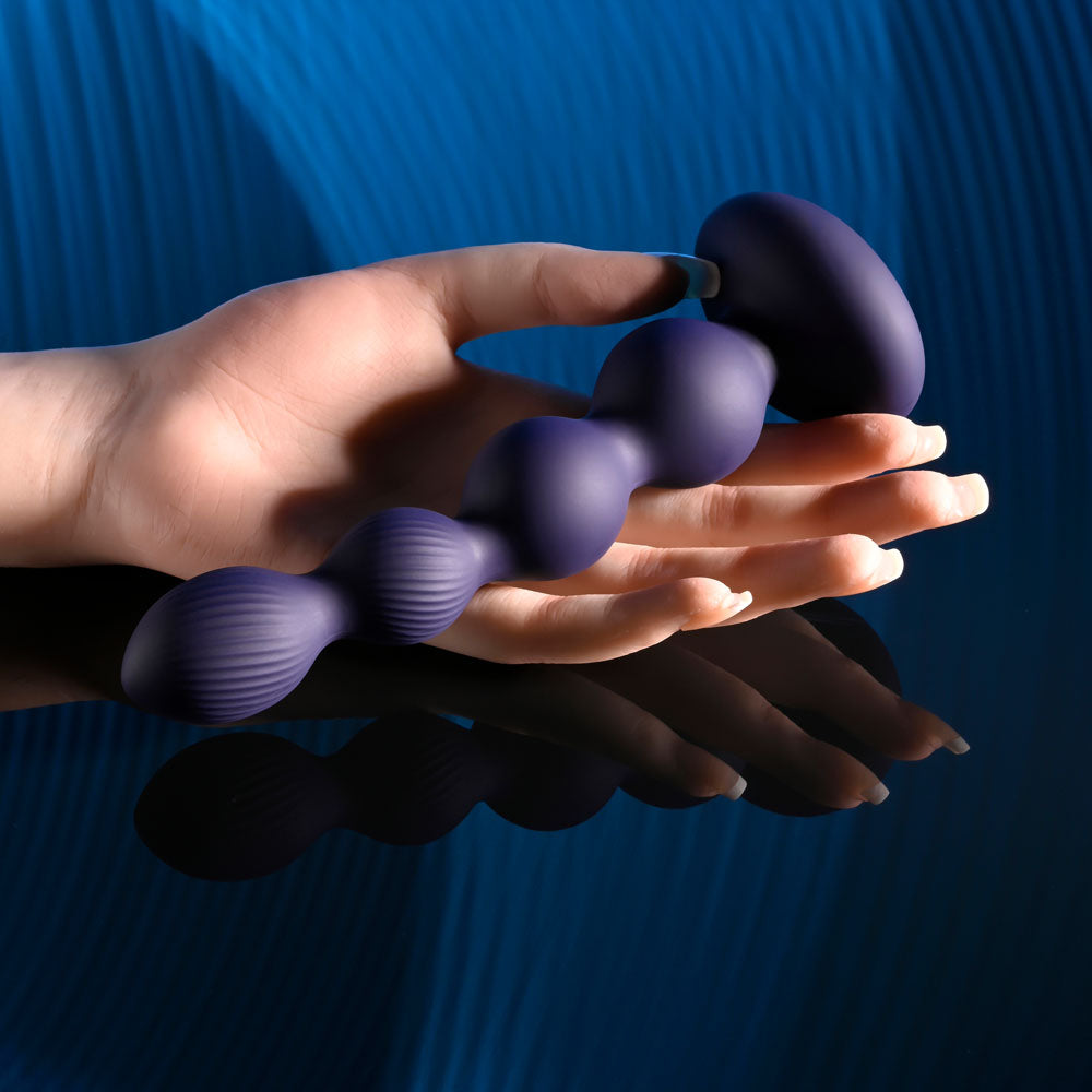 Evolved PLEASURE ORBIT - Navy  17.8 cm USB Rechargeable Twirling & Vibrating Anal Beads with Remote held in a hand.