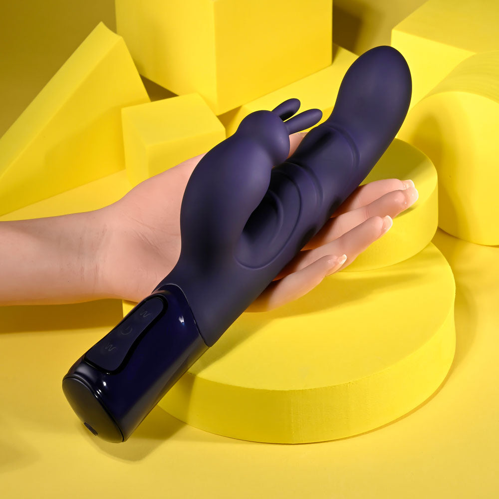 Evolved BIG DEAL - 25.7 cm USB Rechargeable Rabbit Vibrator held in hand against yellow geometric shapes.