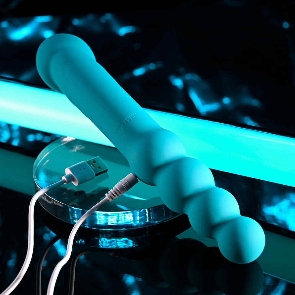 Evolved FLIP FLOP - 23.1 cm USB Rechargeable Dual Ended Vibrator in vibrant turquoise charging on a sleek surface.