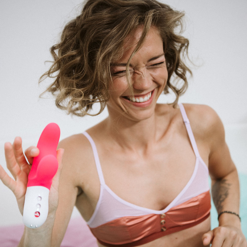 Woman smiling while holding Fun Factory MISS BI - 17 cm USB Rechargeable Rabbit Vibrator, showcasing intimate essentials for her.