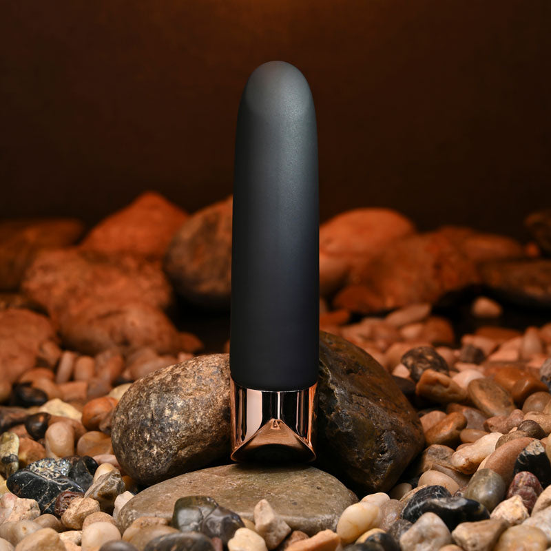 Gender X THE GOLD STANDARD - /Rose Gold 10 cm USB Rechargeable Bullet positioned on stones for intimate essentials.