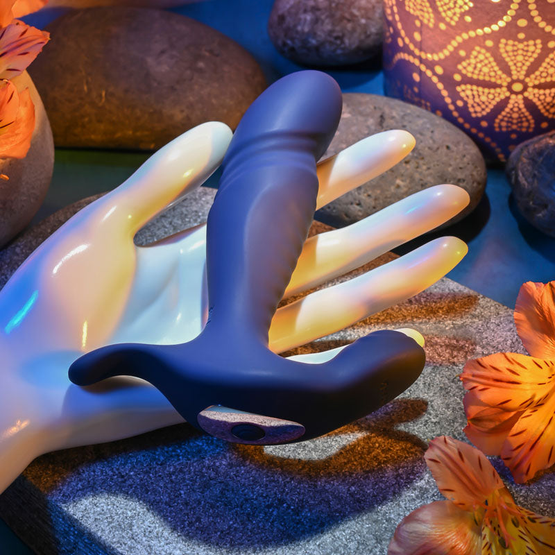 Gender X TRUE -  13.5 cm USB Rechargeable Thrusting Prostate Massager on a hand with decorative stones and flowers.