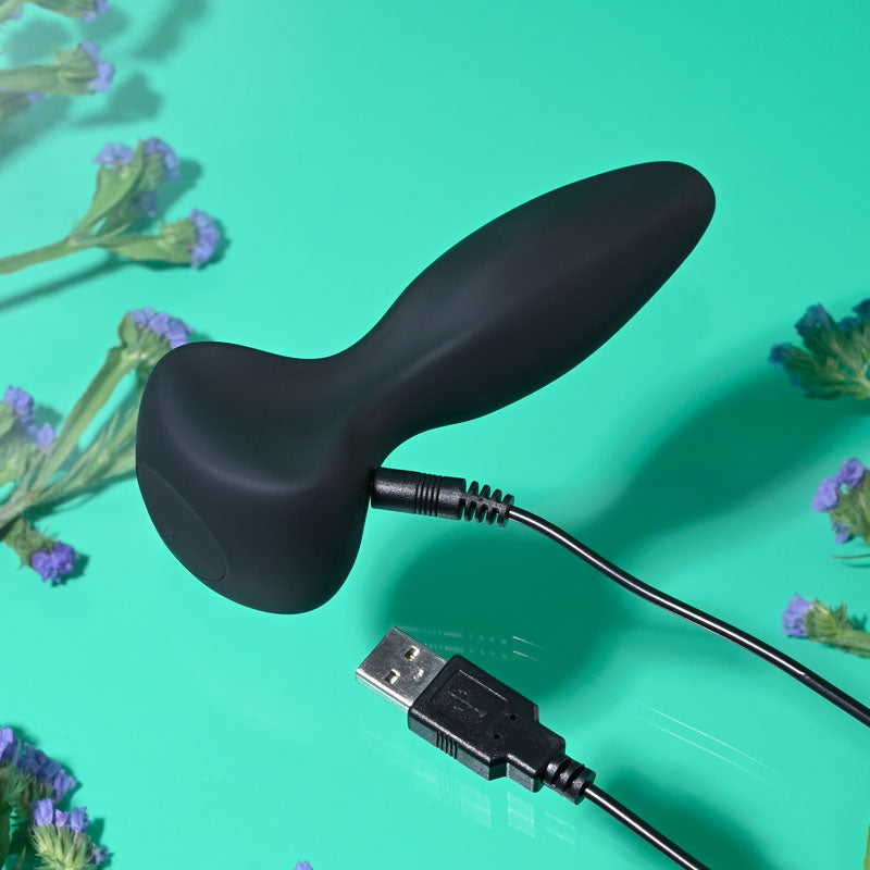 Gender X HIP TO BE SQUARE - black silicone vibrator with USB charging on a vibrant green background.
