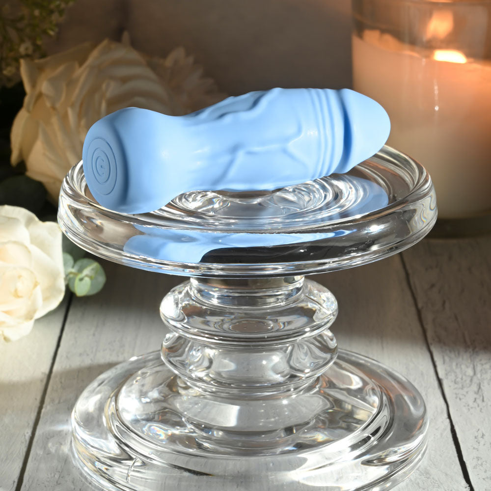Gender X LIL BUDDY - Light 10.1 cm USB Rechargeable Mini Vibrator resting on a glass pedestal with candles and flowers.
