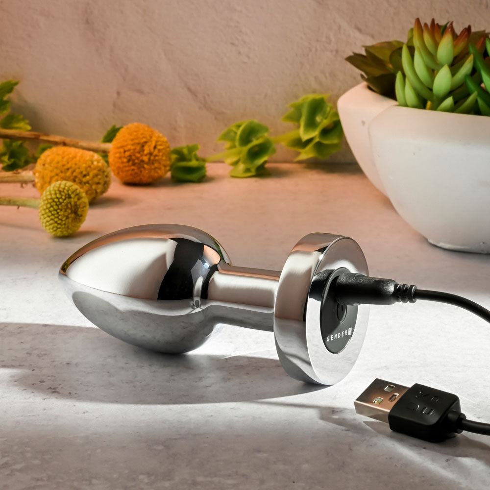 Gender X ROCKIN METAL PLUG XL - 10.5 cm USB Rechargeable Vibrating XL Butt Plug charging on a sleek surface.