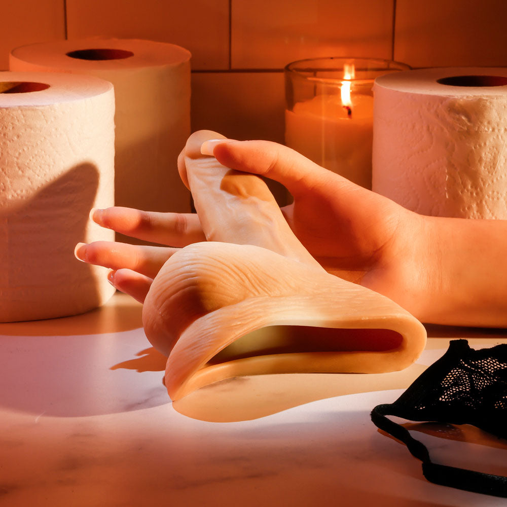 Gender X STAND TO PEE - Light - Realistic Stand-To-Pee Funnel held in hand with paper towels and candle in background.