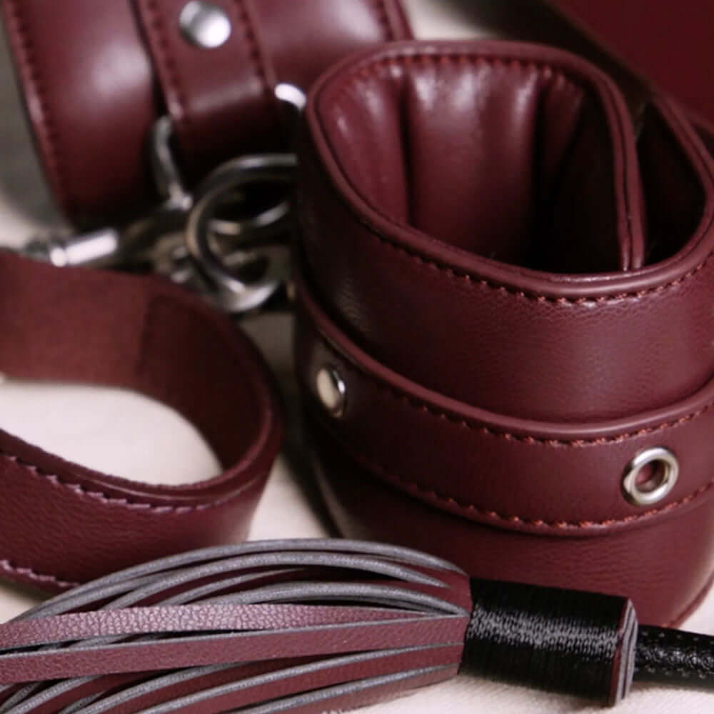 Close-up of a burgundy beginner bondage kit featuring padded cuffs and a double-ended crop.