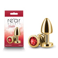Rear Assets Petite - Gold with Red Gem - Gold 6 cm Metal Butt Plug with Red Round Gem Base next to packaging.