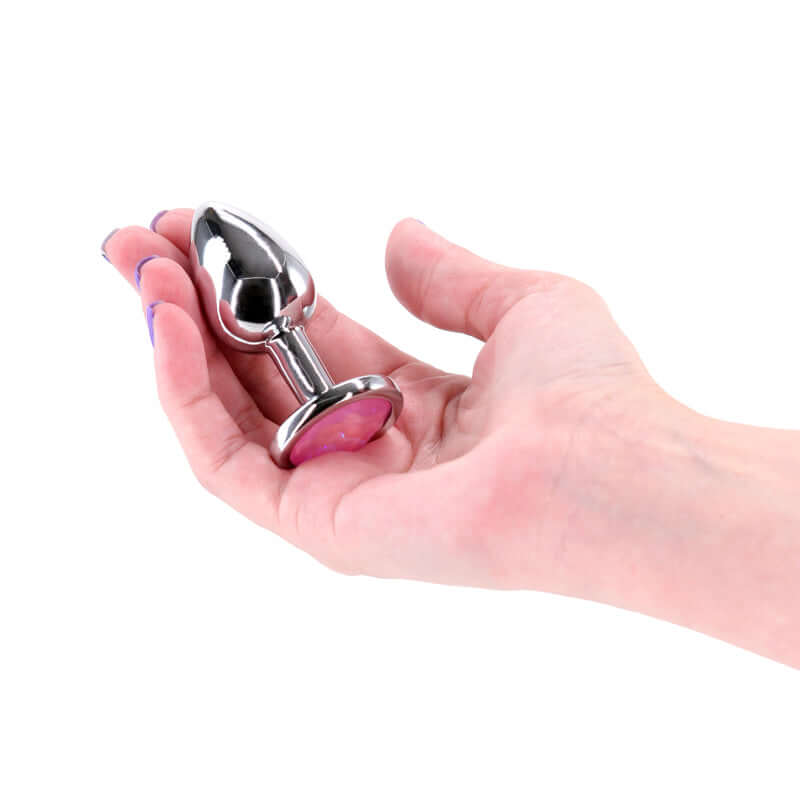 A person holding a small metal butt plug with pink gem in their hand, showcasing its chrome-plated design.