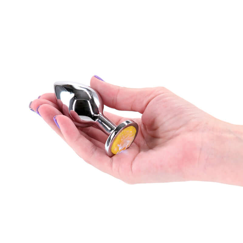 Silver medium metal butt plug with yellow gem base held in a hand, showcasing yellow gem aluminum butt plug.