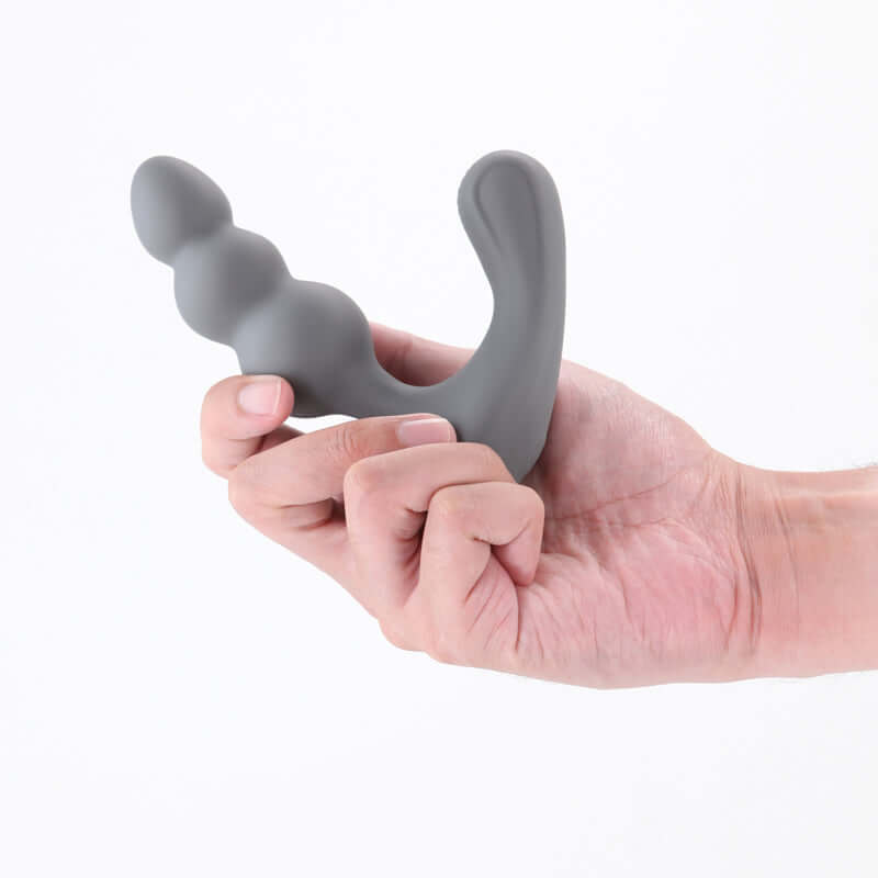 Hand holding the Renegade Thumper, a grey USB rechargeable prostate massager with beaded shaft design.
