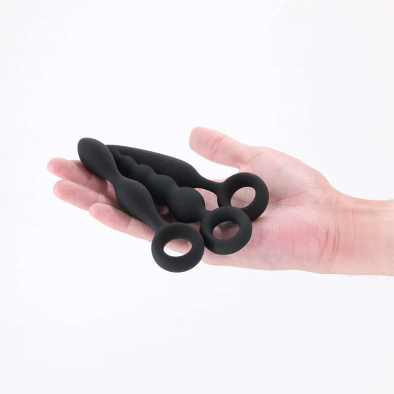 Beginner anal plug set in a hand, featuring three body-safe silicone plugs with finger rings for easy retrieval.