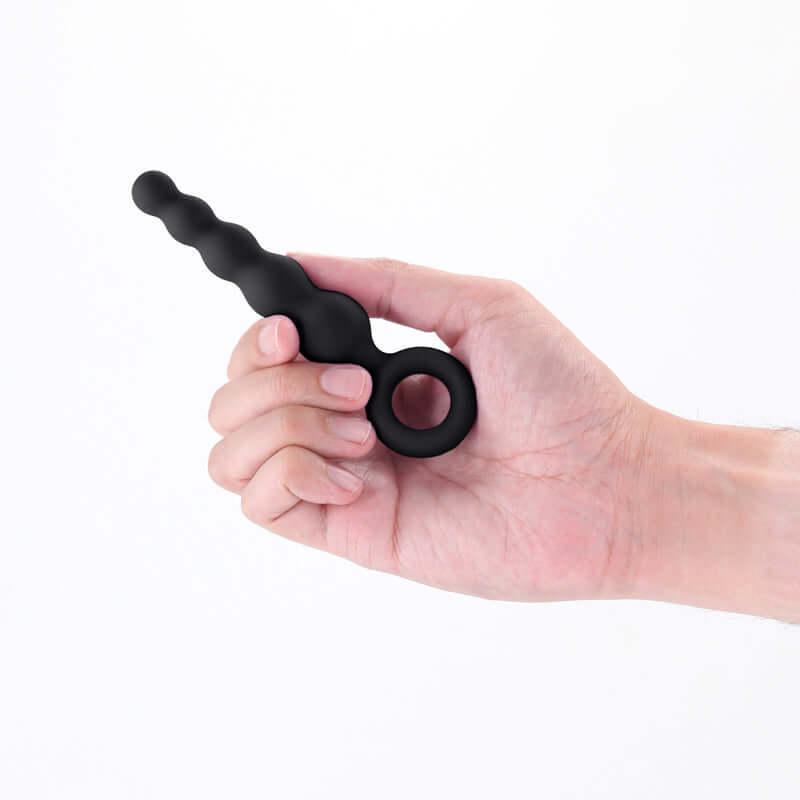 Beginner silicone anal plug held in hand, featuring a tapered design and finger ring for comfort and control.