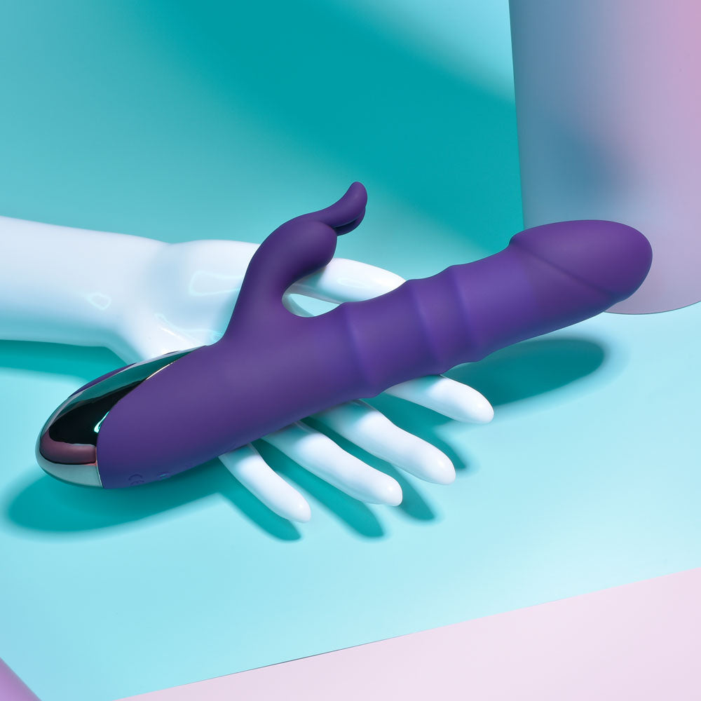 Playboy Pleasure HOP TO IT -  23.5 cm USB Rechargeable Rabbit Vibrator on a hand with a colorful background.