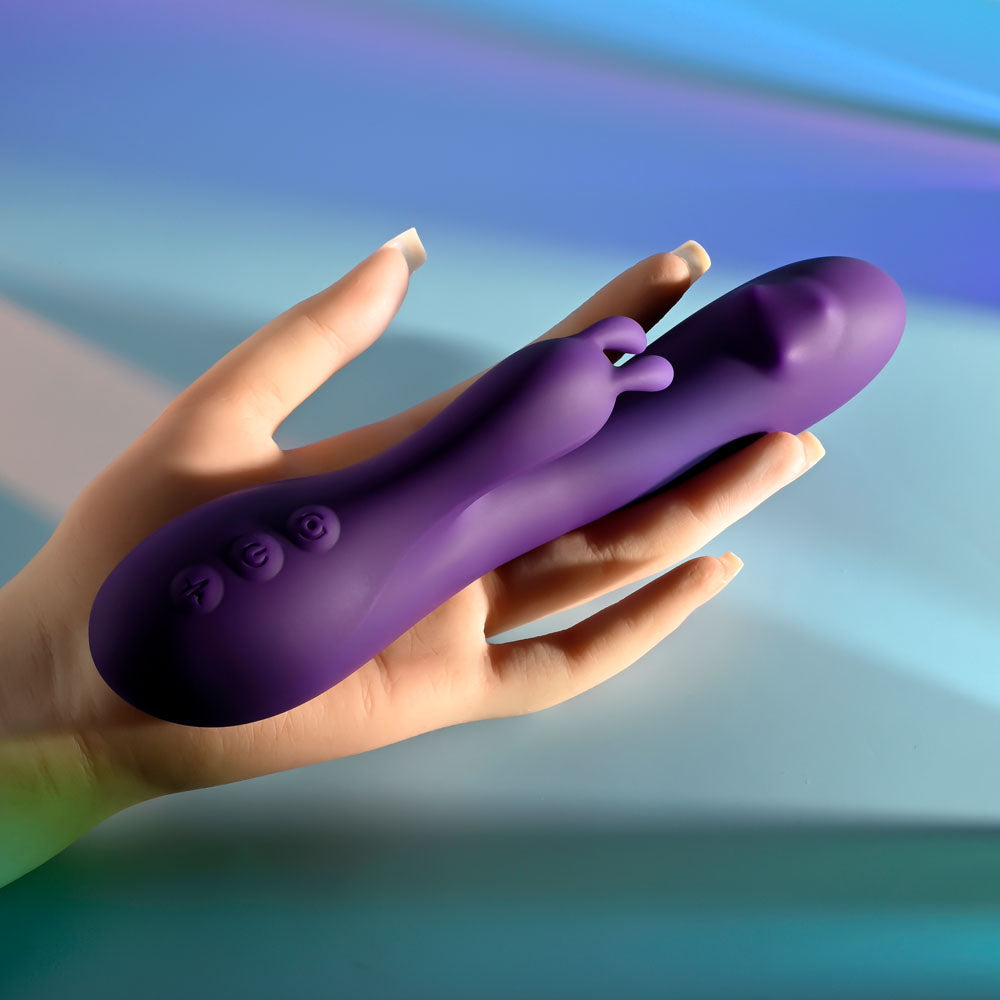 Playboy Pleasure ON REPEAT - 19.7 cm USB Rechargeable Rabbit Vibrator held in hand against a colorful background.