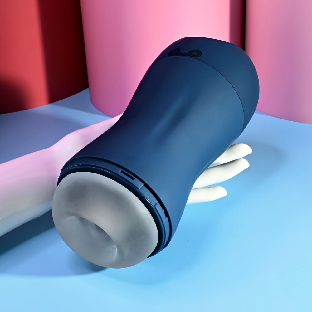 Playboy Pleasure GUSTO - USB Rechargeable Vibrating & Sucking Masturbator held in a hand against a colorful background.