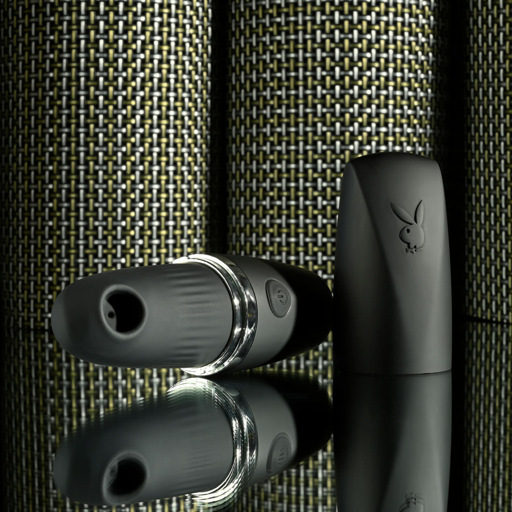 Playboy Pleasure EXCURSION USB rechargeable suction stimulator on reflective surface with stylish case.