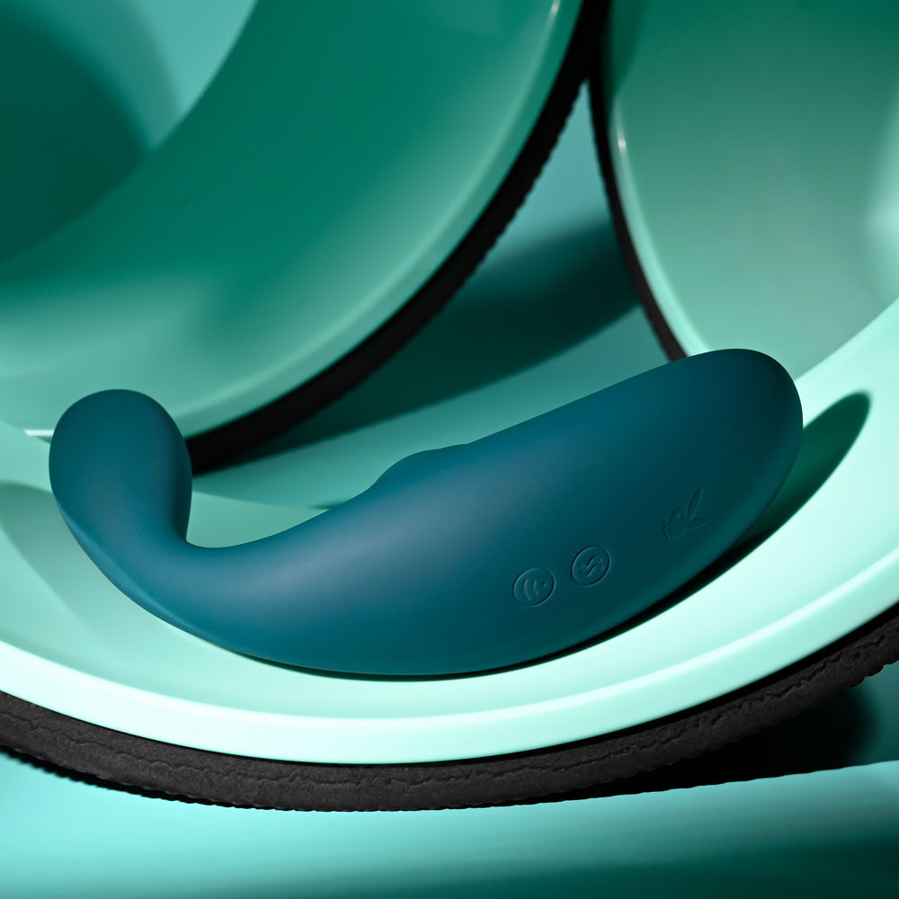 Playboy Pleasure CHARMER -  USB Rechargeable Vibrator with Clitoral Suction on a soft surface.