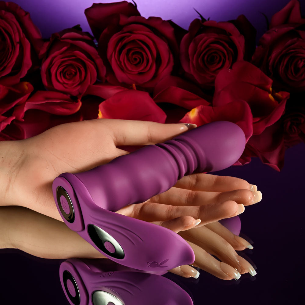 Playboy Pleasure MATCH PLAY - USB Rechargeable with C-Ring Attachment surrounded by red roses and held in a hand.