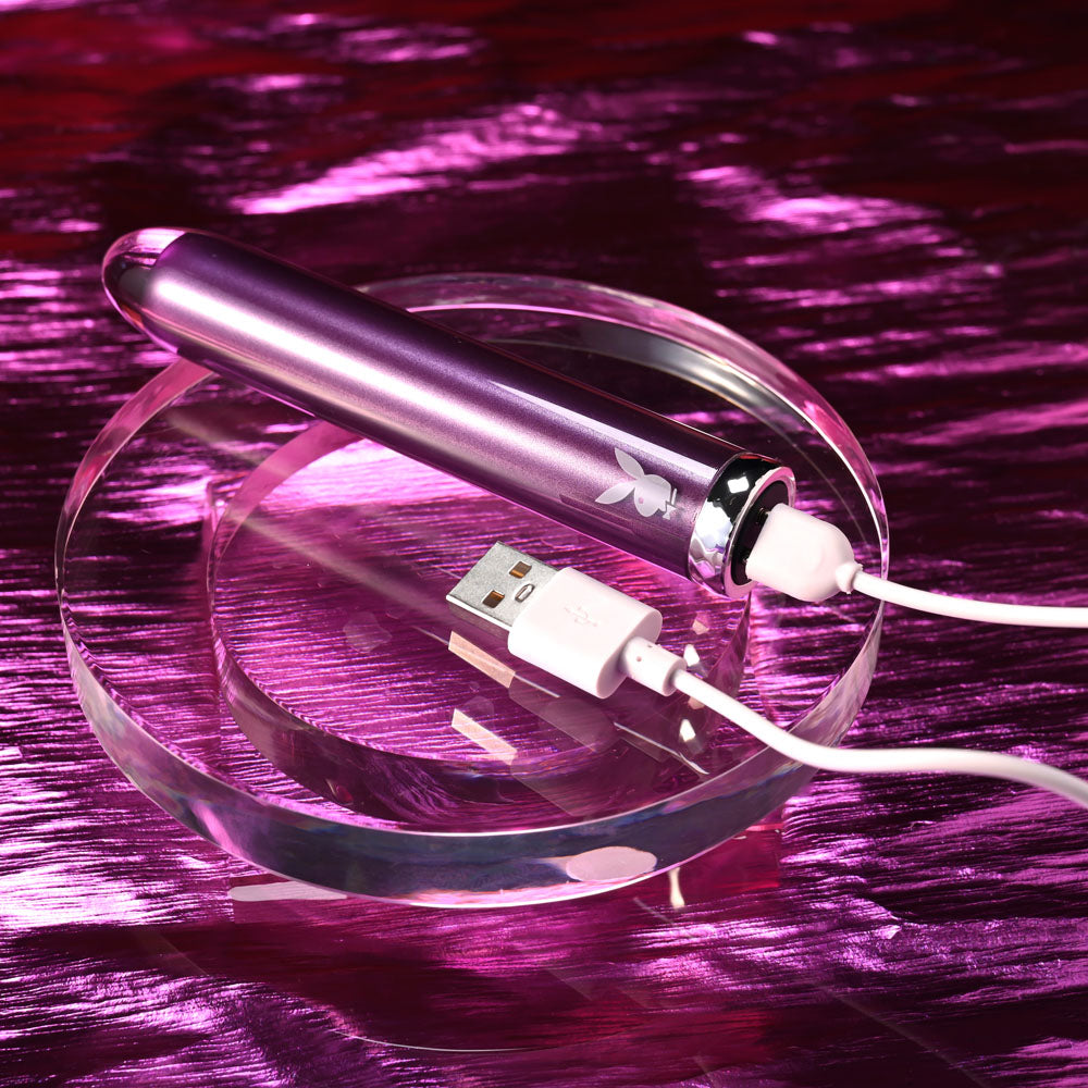 Playboy Pleasure AMETHYST - 12.4 cm USB Rechargeable Glass Tipped Mini Vibrator on a clear dish with charging cable.