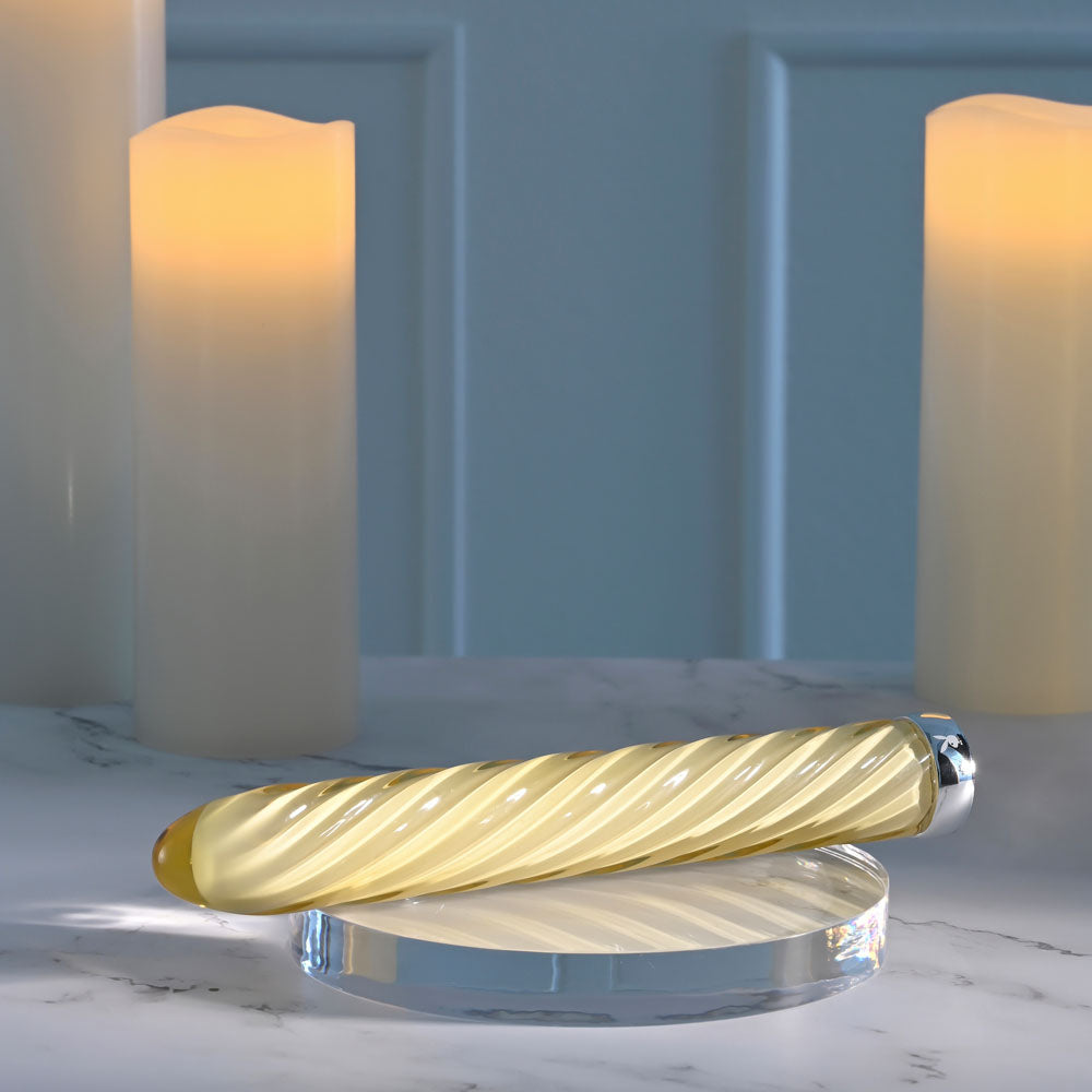 Playboy Pleasure TWIST OF FATE - Glass 17.5 cm USB rechargeable glass vibrator on a marble surface with candles.