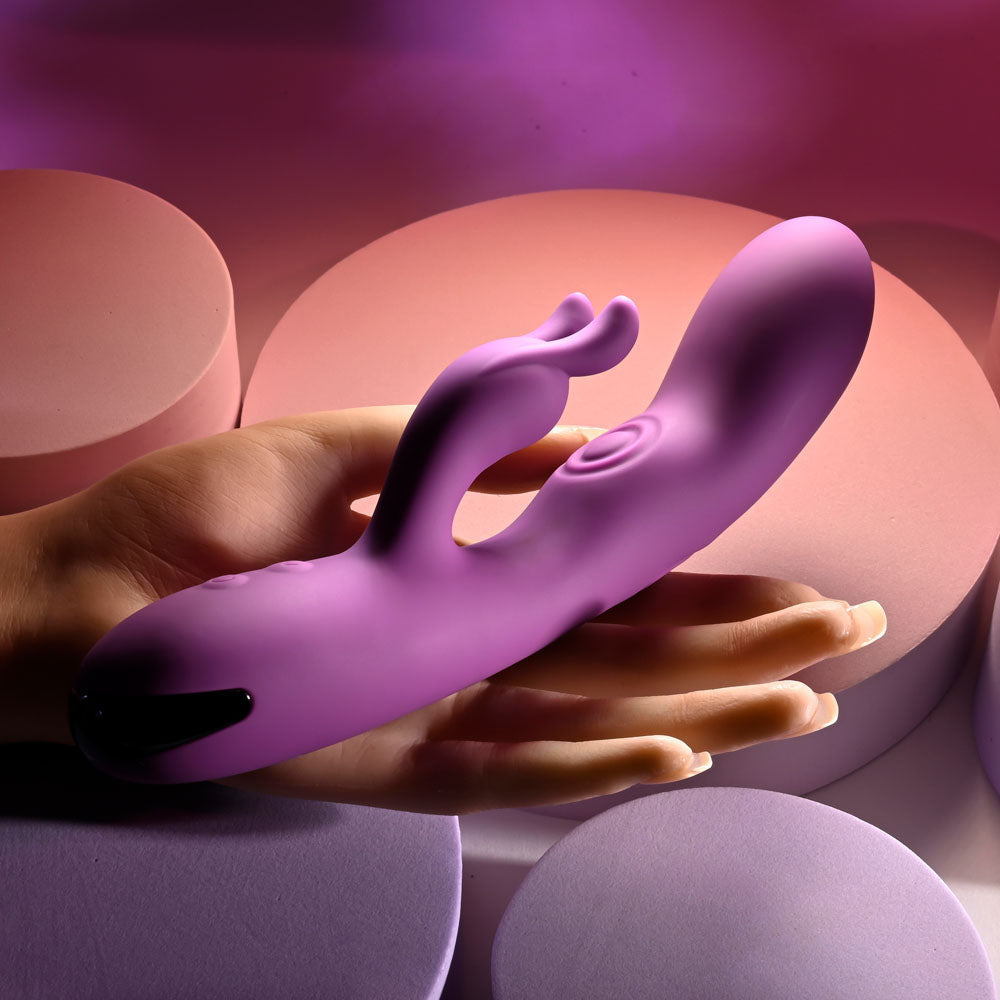 Playboy Pleasure BUSY BUNNY - 22.6 cm USB Rechargeable Rabbit Vibrator with Tapping Shaft in a hand on soft background.