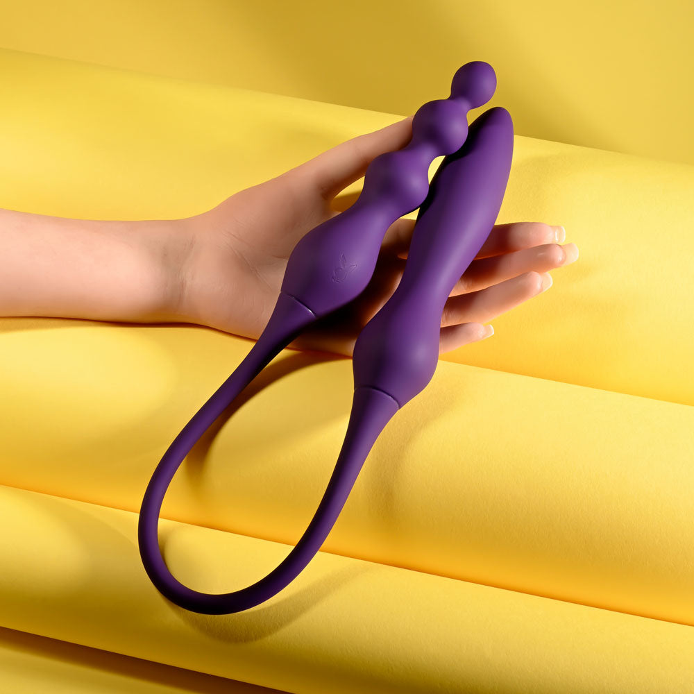 Playboy Pleasure THIS & THAT -  60 cm USB Rechargeable Flexible Dual Ended Vibrator on a hand against a yellow background.