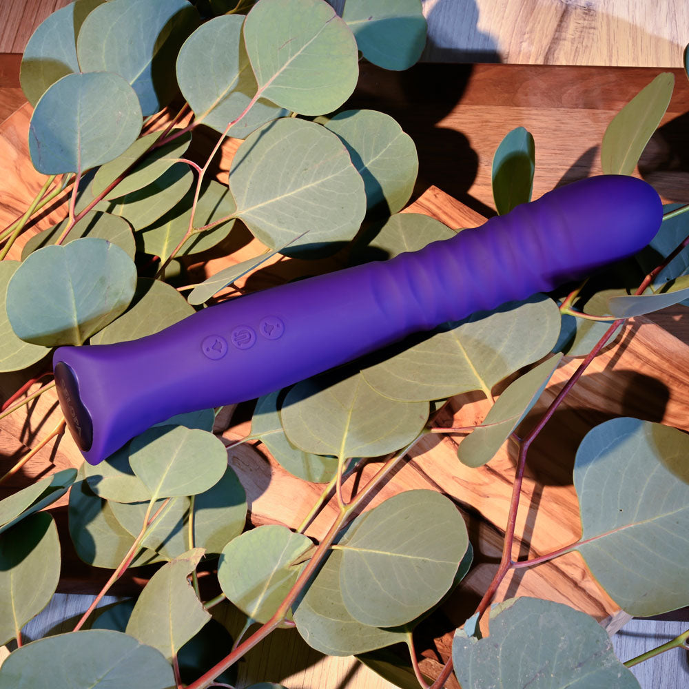 Selopa TRIXXXIE - 22.2 cm USB Rechargeable Vibrator on a wooden surface surrounded by eucalyptus leaves.