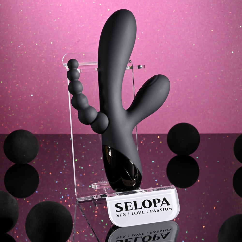 Selopa TRIPLE ACES - 19.7 cm USB Rechargeable Triple Stimulator Vibrator displayed on a stand with a pink sparkle background.