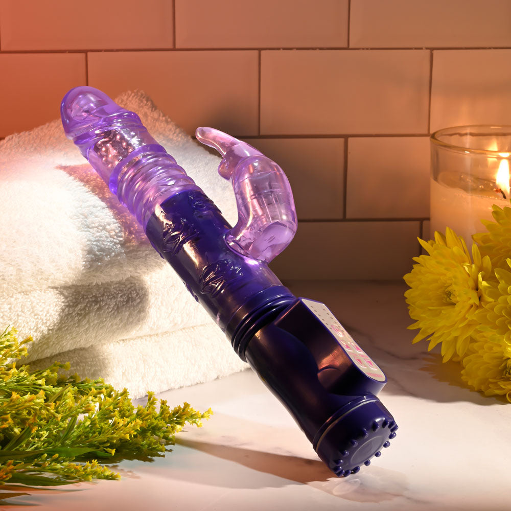 Selopa BUNNY THRUSTER -  24.8 cm Thrusting Rabbit Vibrator displayed on a towel with flowers and candles.