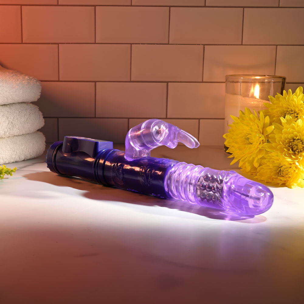Selopa BUNNY THRUSTER - 24.8 cm Thrusting Rabbit Vibrator on a bathroom counter with towels and flowers.