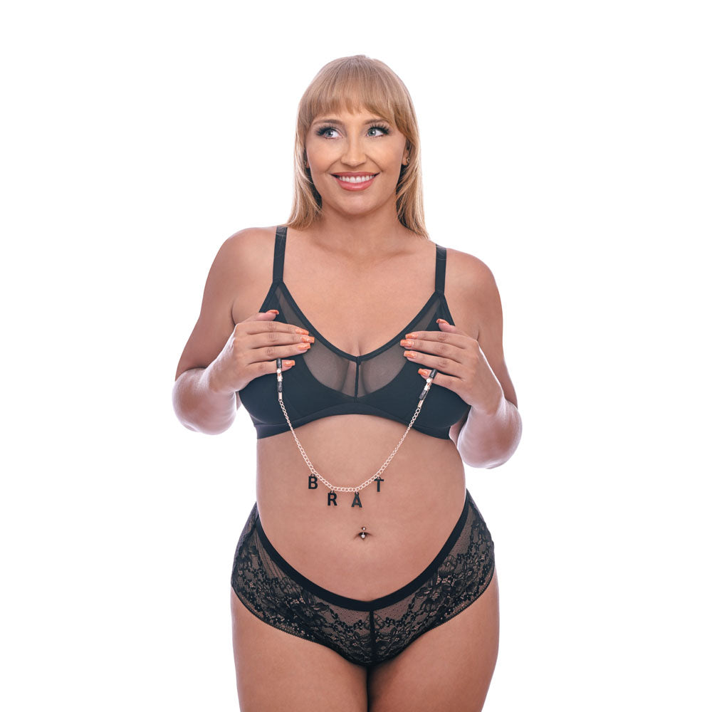 Model wearing black lingerie with 'BRAT' chain, showcasing Sex & Mischief Brat Charmed Nipple Clamps - Nipple Clamps with 45 cm Chain.