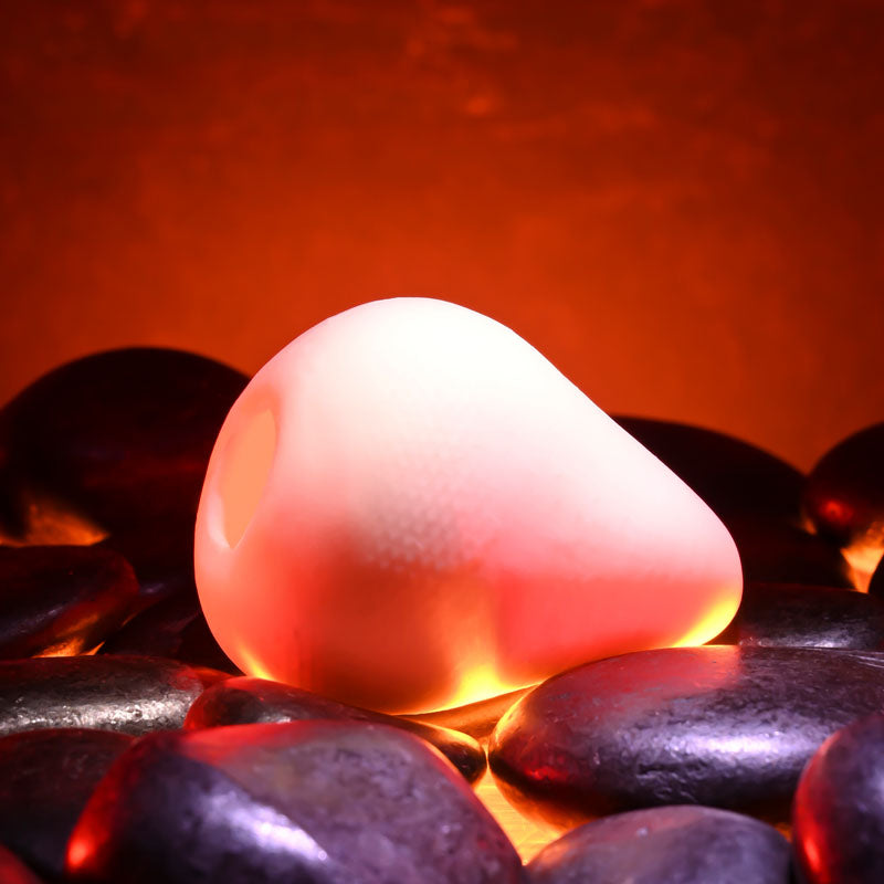 Zero Tolerance FUJI -  Mini Stroker Egg resting on smooth stones with a warm glow, showcasing its soft and flexible design.
