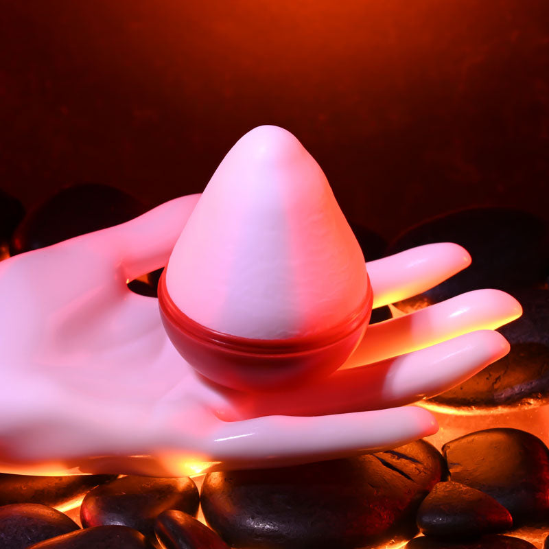 Zero Tolerance FUJI - Mini Stroker Egg held in a hand with glowing stones in the background for intimate essentials.